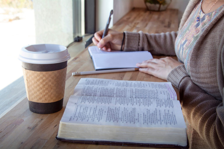 Woman writing in a notebook with an open Bible and a coffee